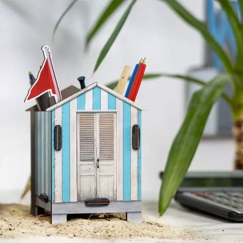 A decorative beach house pen pot with placed on a desk next to a plant and a calculator.