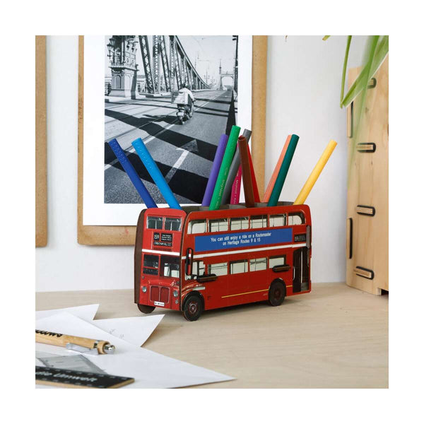Red double-decker bus-shaped pen holder with colorful pens on a desk.