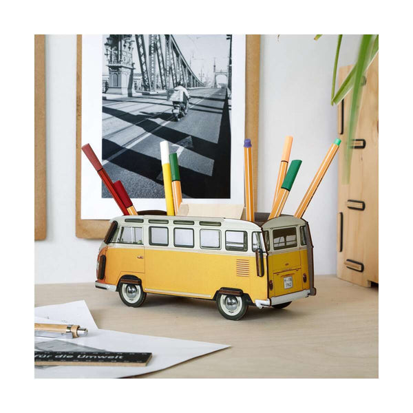 Yellow van-shaped pen holder with colorful pens on a desk.