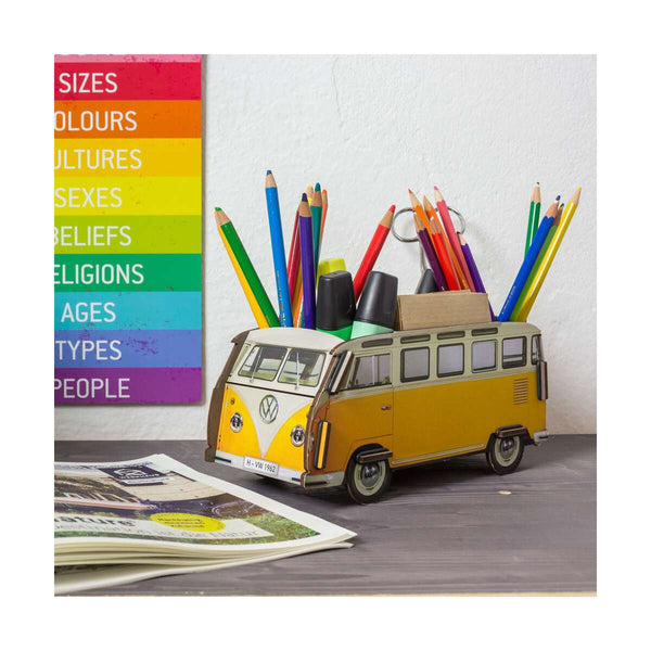 Yellow Volkswagen van with colourful pencils and a rainbow-coloured poster on a gray surface.