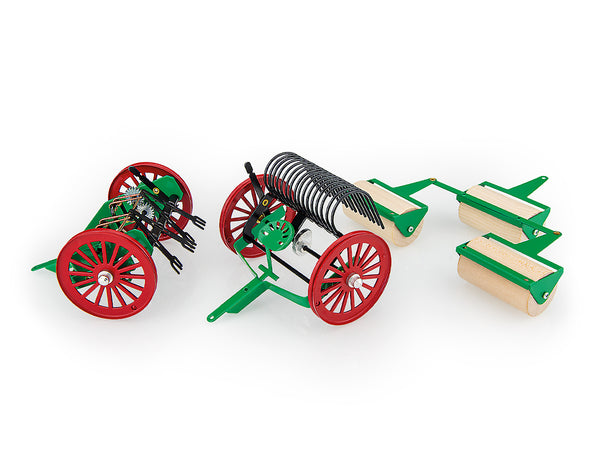 A set of toy tractor accessories including a tedder, rake, and wooden rollers, predominantly green and red in colour.