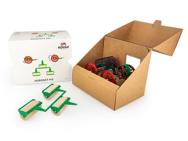A set of toy tractor accessories including a tedder, rake, and wooden rollers, predominantly green and red in colour, with the box displayed