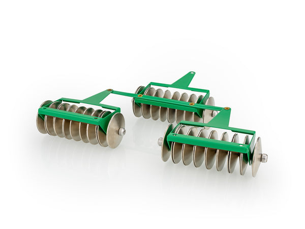 A set of toy rotavators with green handles and silver-coloured rollers, set against a white background.